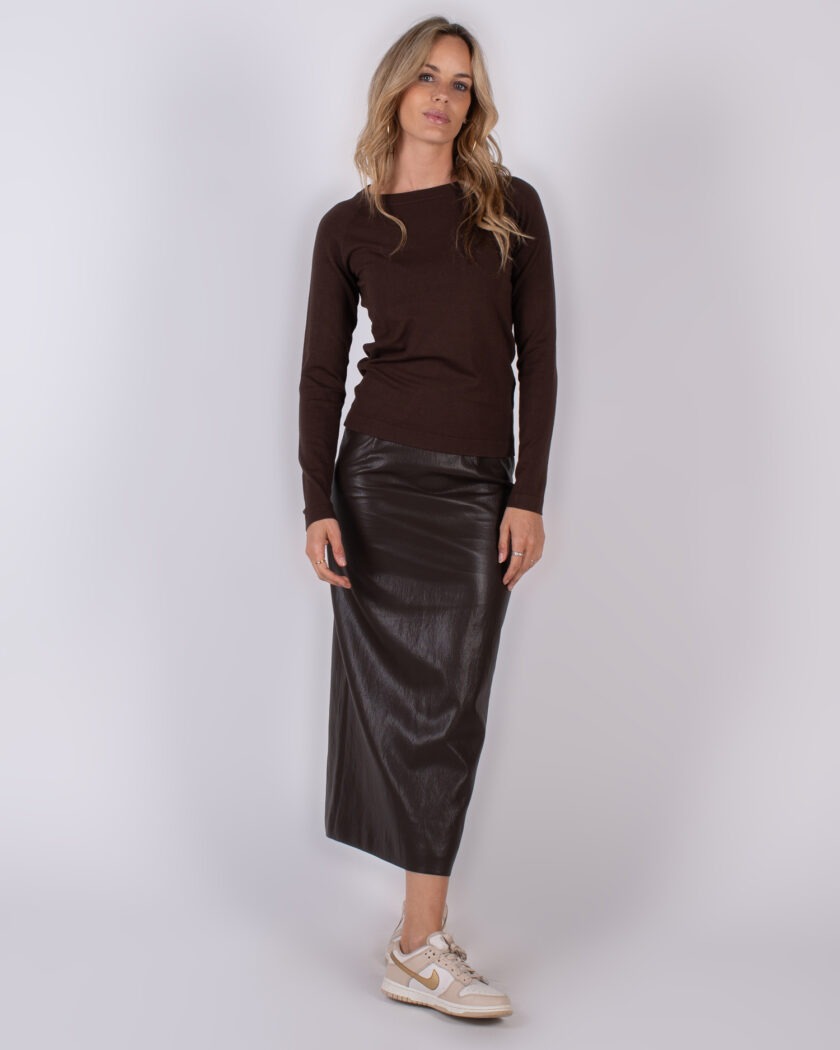 Vrouw gekleed in een donkerbruine trui en een lange, glanzende lederen rok met beige sneakers.