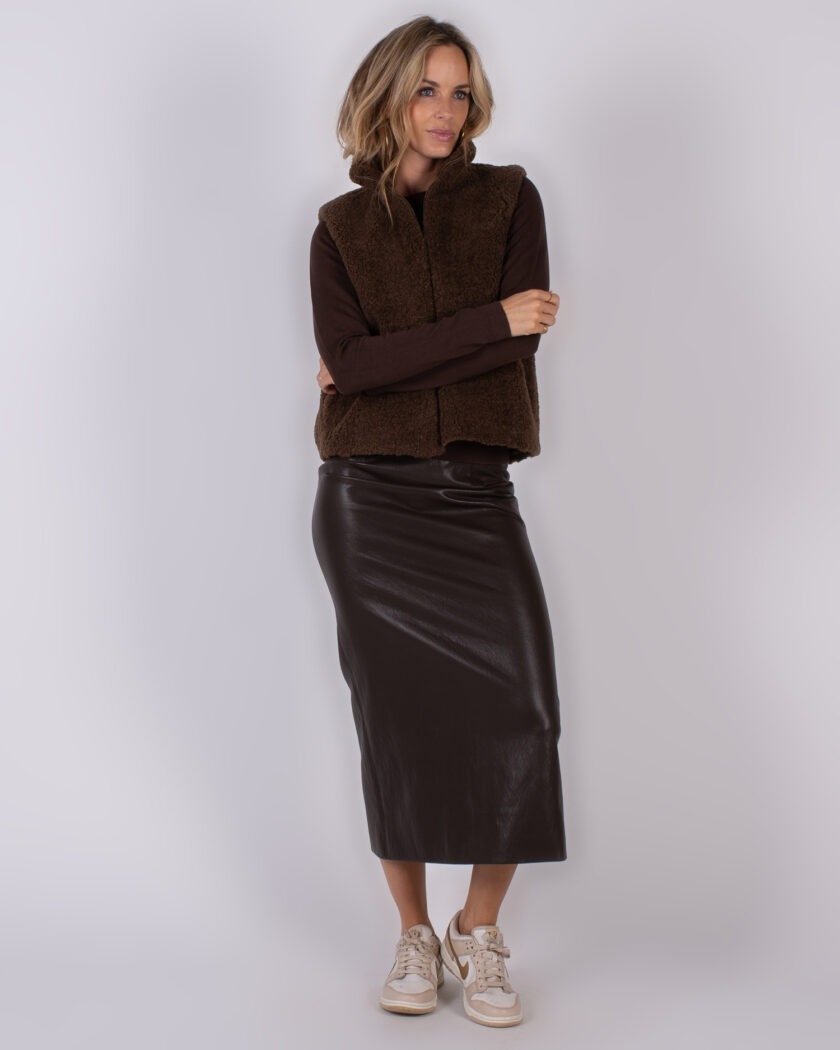 Vrouw in een bruine teddy bodywarmer, donkerbruine top en lange leren rok uit de Studio AW25-26 collectie.