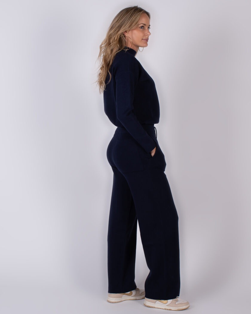 Vrouw in marineblauwe lounge-set met wijde broek en sneakers in zijaanzicht.