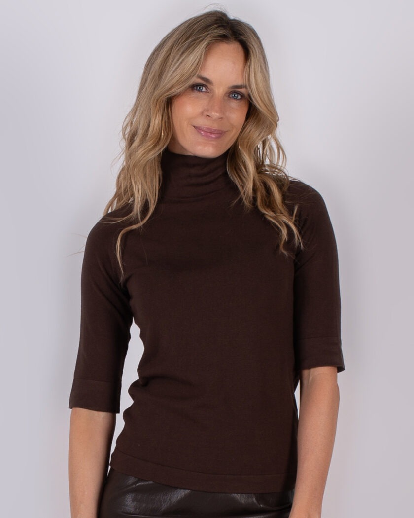 Vrouw met lang blond haar draagt een donkerbruine coltrui met halve mouwen uit de Studio AW25-26 collectie.