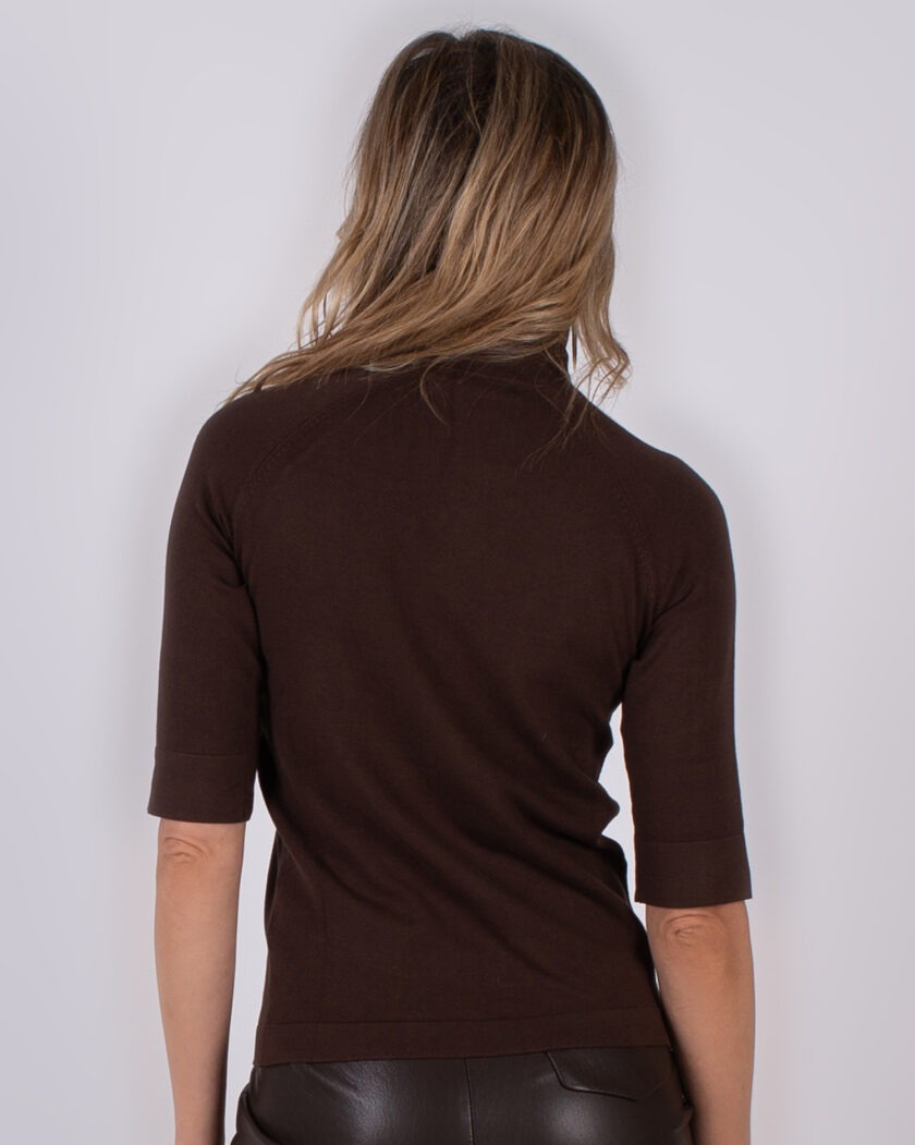 Achteraanzicht van een vrouw in een donkerbruine top met halve mouwen en een bruine leren broek.