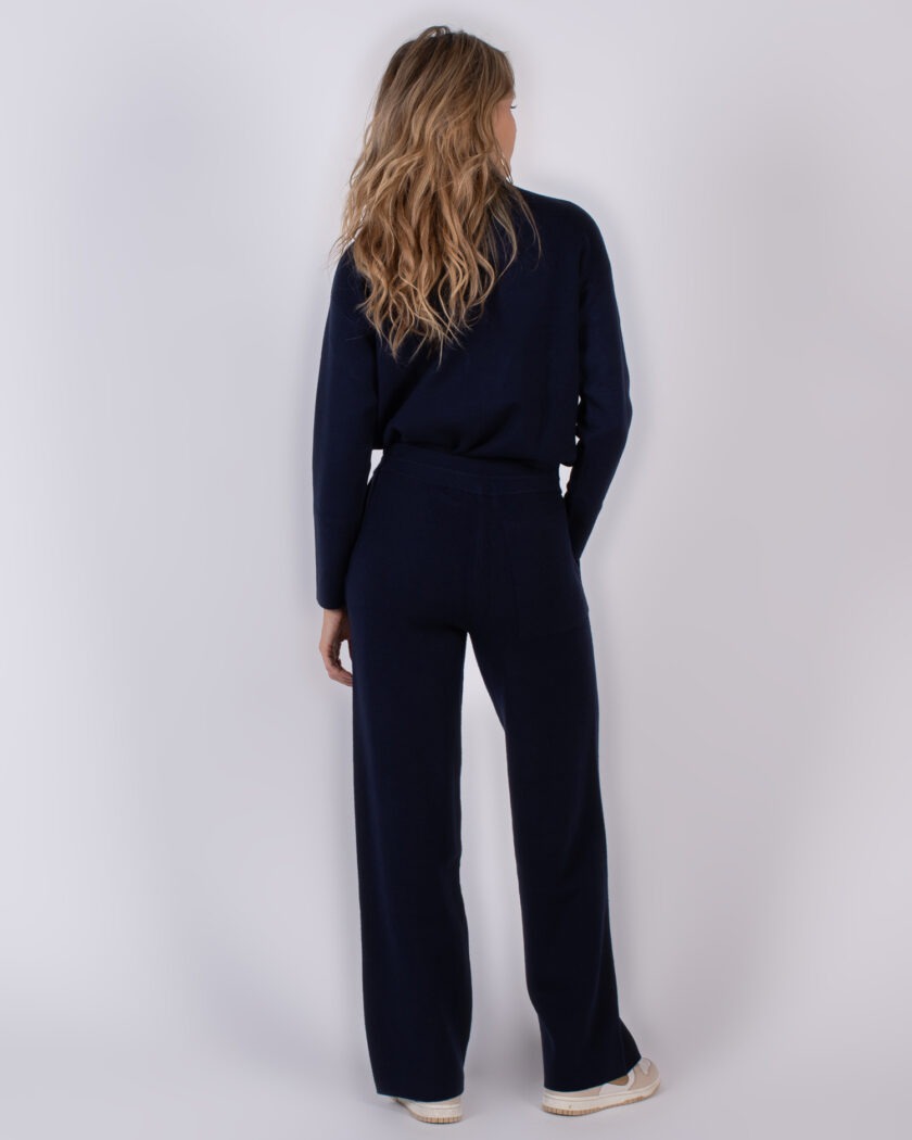 Vrouw gekleed in een donkerblauwe loungewear-set, staand met de rug naar de camera.