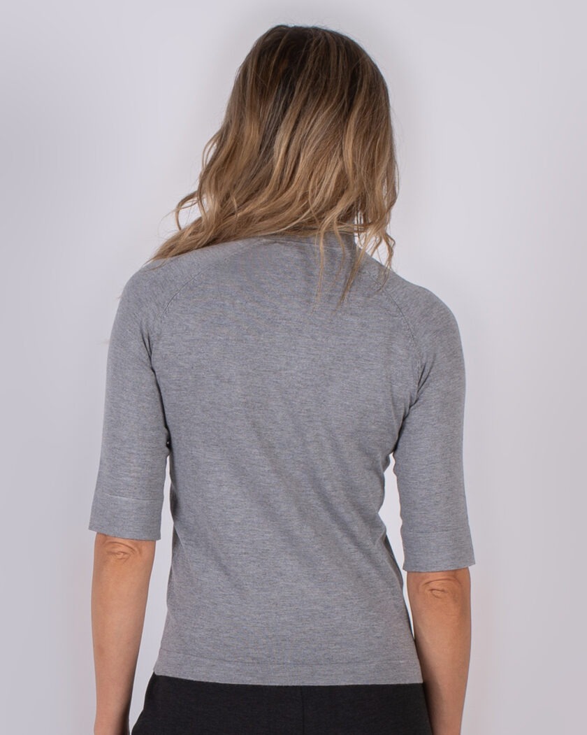 Vrouw met los haar draagt een grijs, half mouw shirt en is van achteren gefotografeerd tegen een neutrale achtergrond.