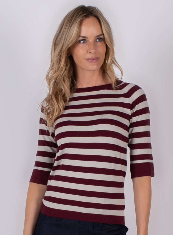 Vrouw met lang blond haar draagt een bordeauxrood met beige gestreepte top met driekwart mouwen.