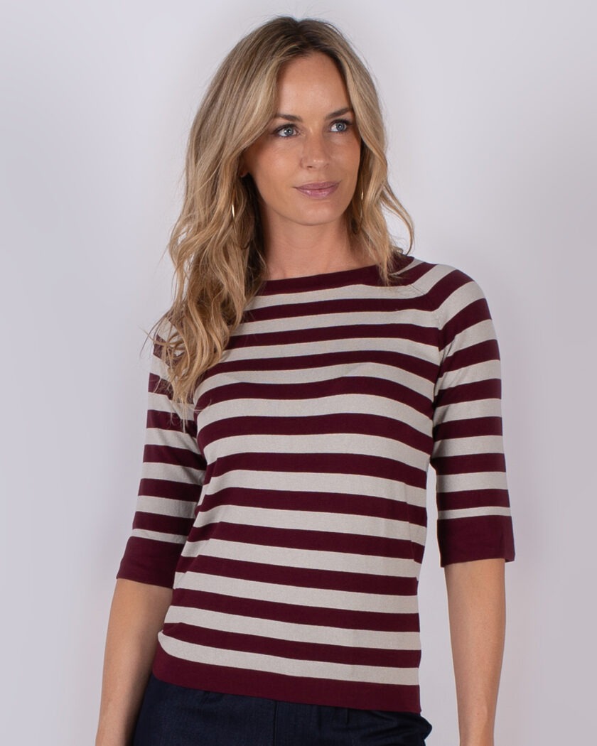 Vrouw met lang blond haar draagt een bordeauxrood met beige gestreepte top met driekwart mouwen.