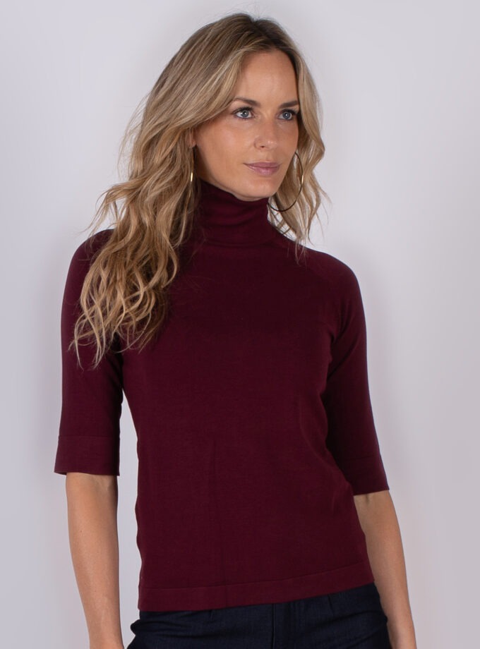 Vrouw draagt een bordeauxrode coltrui met halve mouwen uit de Studio AW25-26 collectie.
