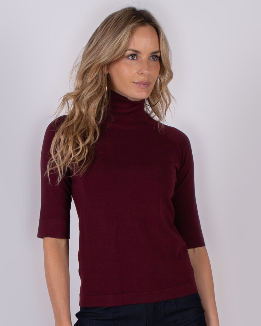 Vrouw draagt een bordeauxrode coltrui met halve mouwen uit de Studio AW25-26 collectie.