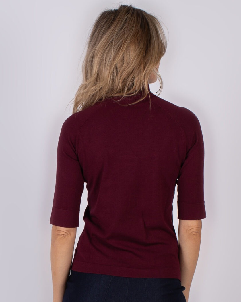 Vrouw van achteren gezien, gekleed in een bordeauxrode top met halve mouwen uit de Studio AW25-26 collectie.