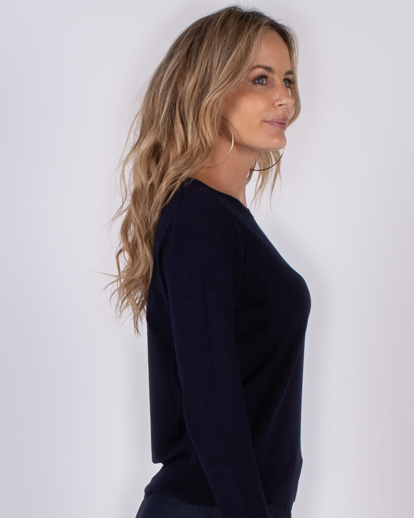 Vrouw in profiel poseert in een donkerblauwe trui uit de Studio AW25-26 collectie.
