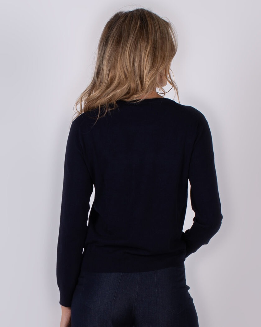 Vrouw met los blond haar draagt een donkerblauwe trui en spijkerbroek, gezien van achteren.