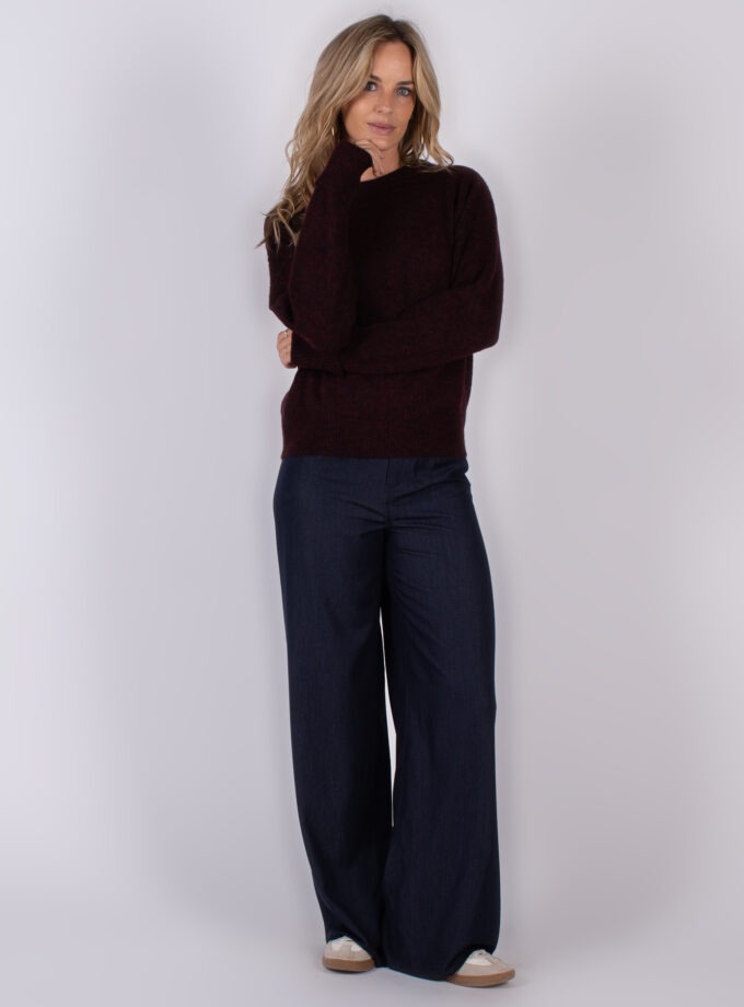 Vrouw draagt een donkerrode trui en wijde donkerblauwe broek uit de Studio AW25-26 collectie.