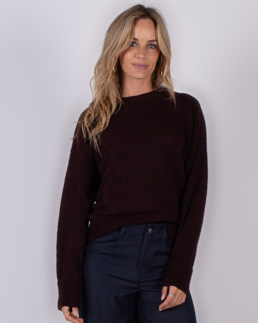 Vrouw draagt een donkerrode trui en een donkerblauwe broek uit de Studio AW25-26 collectie.