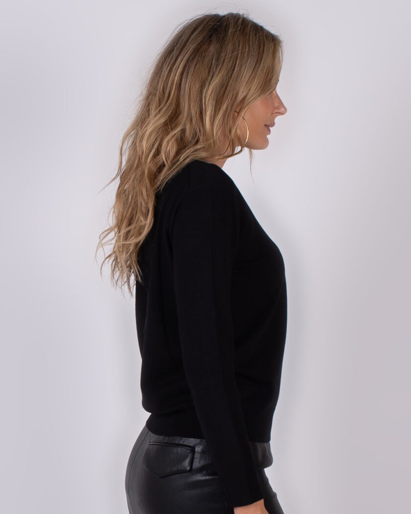 Vrouw in zijaanzicht draagt een zwarte trui en een zwarte leren broek uit de Studio AW25-26 collectie.