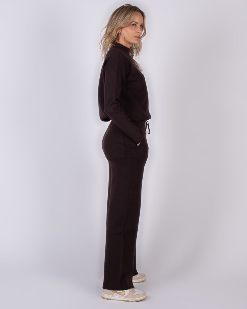 Vrouw in zijaanzicht draagt een donkerbruin loungewearpak uit de Studio AW25-26 collectie.