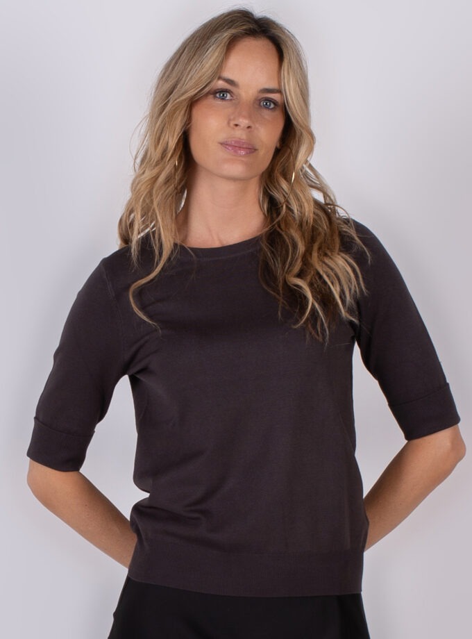 Vrouw met lang blond haar draagt een donkerbruin shirt met halve mouwen uit de Studio AW25-26 collectie.