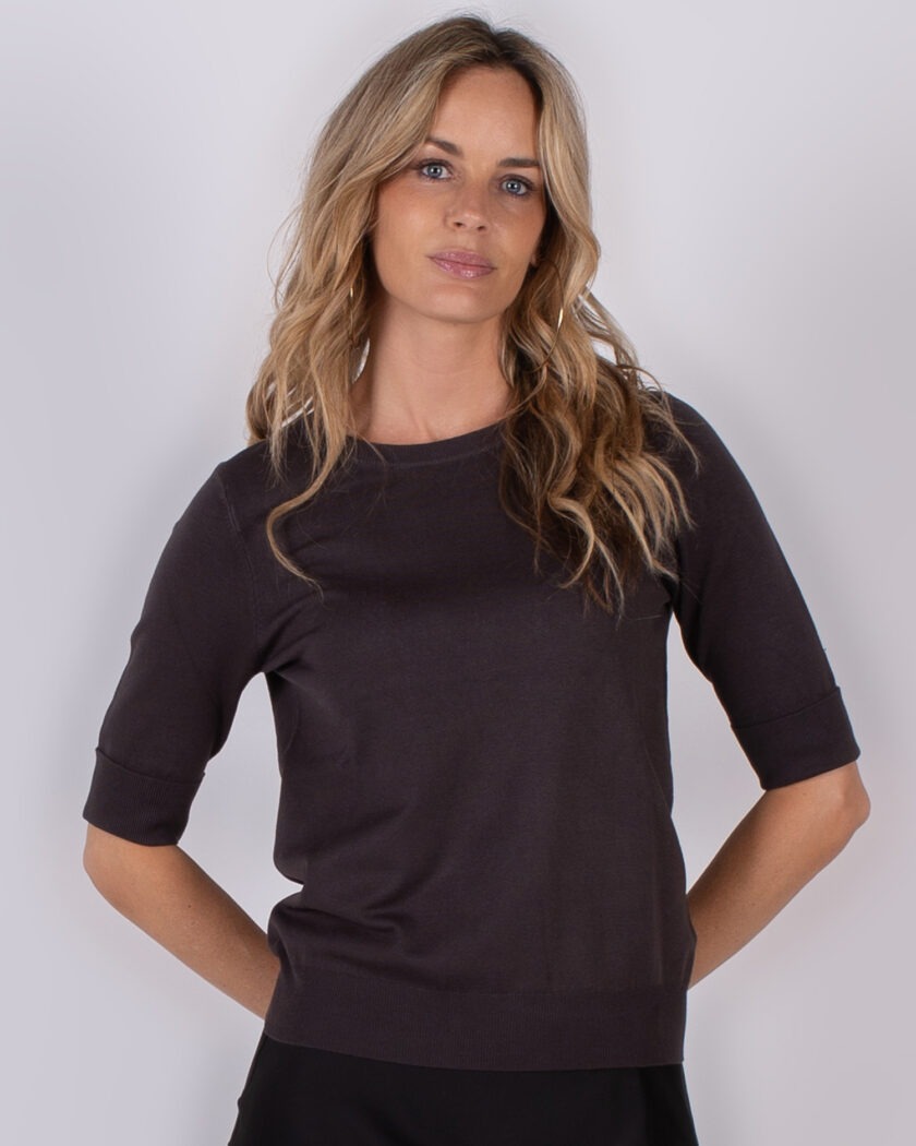 Vrouw met lang blond haar draagt een donkerbruin shirt met halve mouwen uit de Studio AW25-26 collectie.
