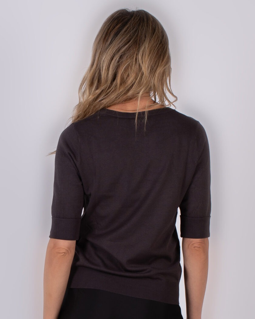 Achteraanzicht van een vrouw die een donkerbruine trui met halflange mouwen draagt uit de Studio AW25-26 collectie.