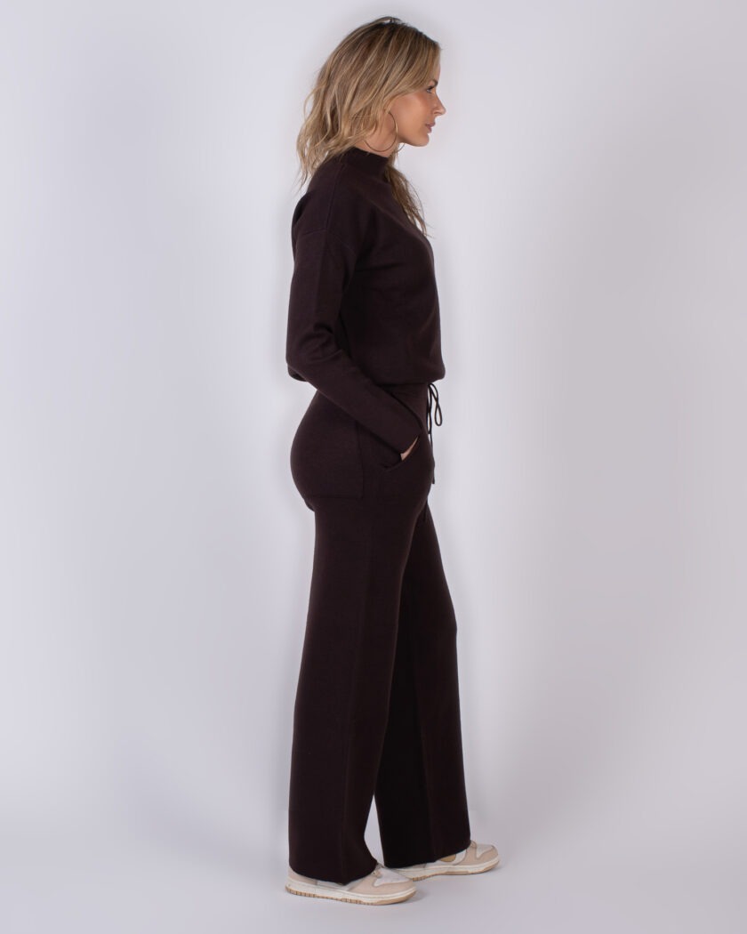 Vrouw in zijaanzicht draagt een donkerbruine, comfortabele loungetset met wijde pijpen uit de Studio AW25-26 collectie.