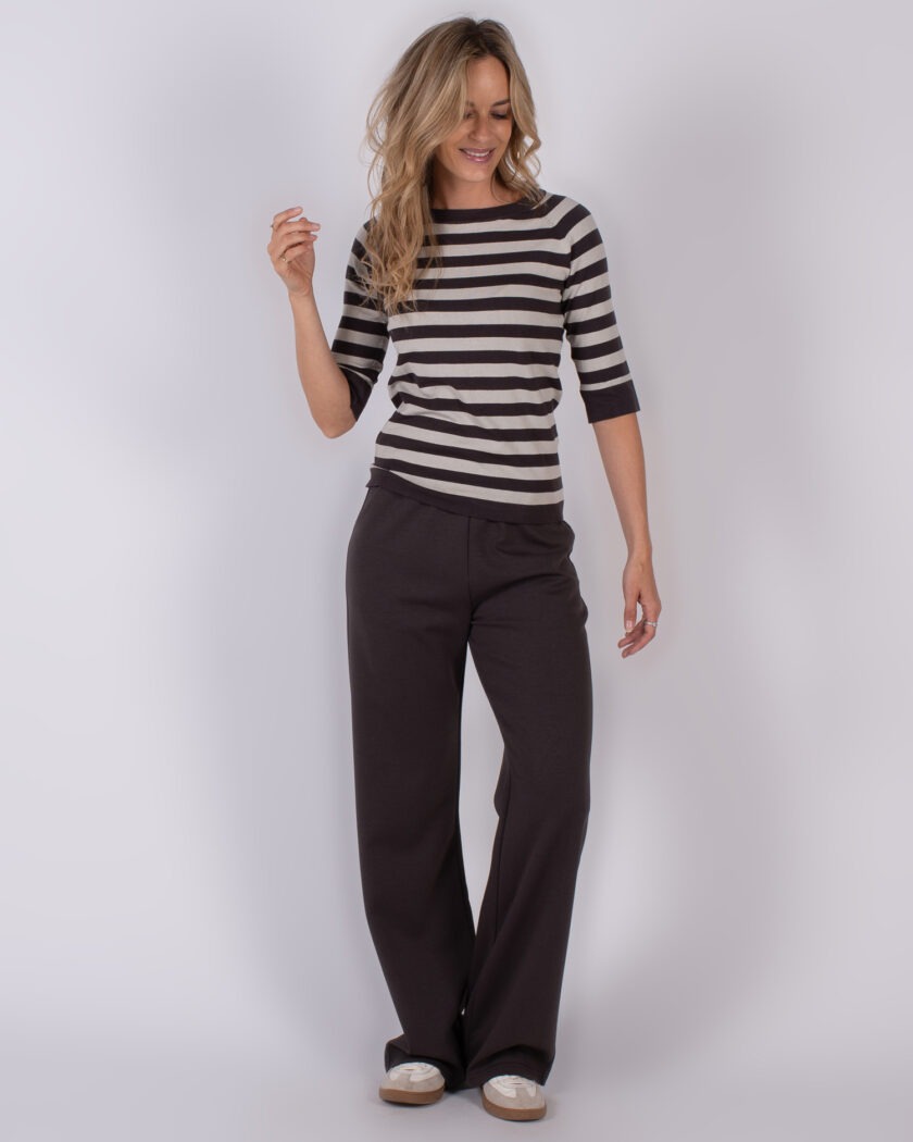 Vrouw in casual outfit met een zwart-grijs gestreepte top en donkere, wijde broek uit Studio_AW25-26 collectie.