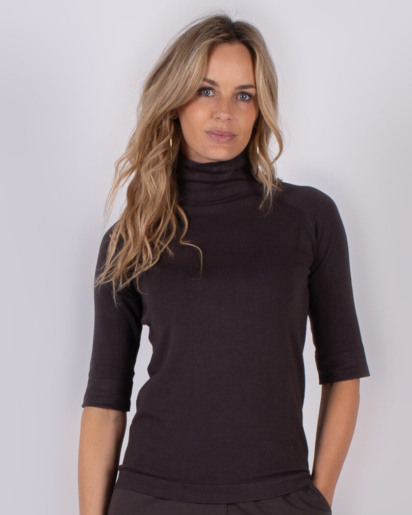 Vrouw draagt een donkerbruine coltrui met halflange mouwen uit de Studio AW25-26 collectie.