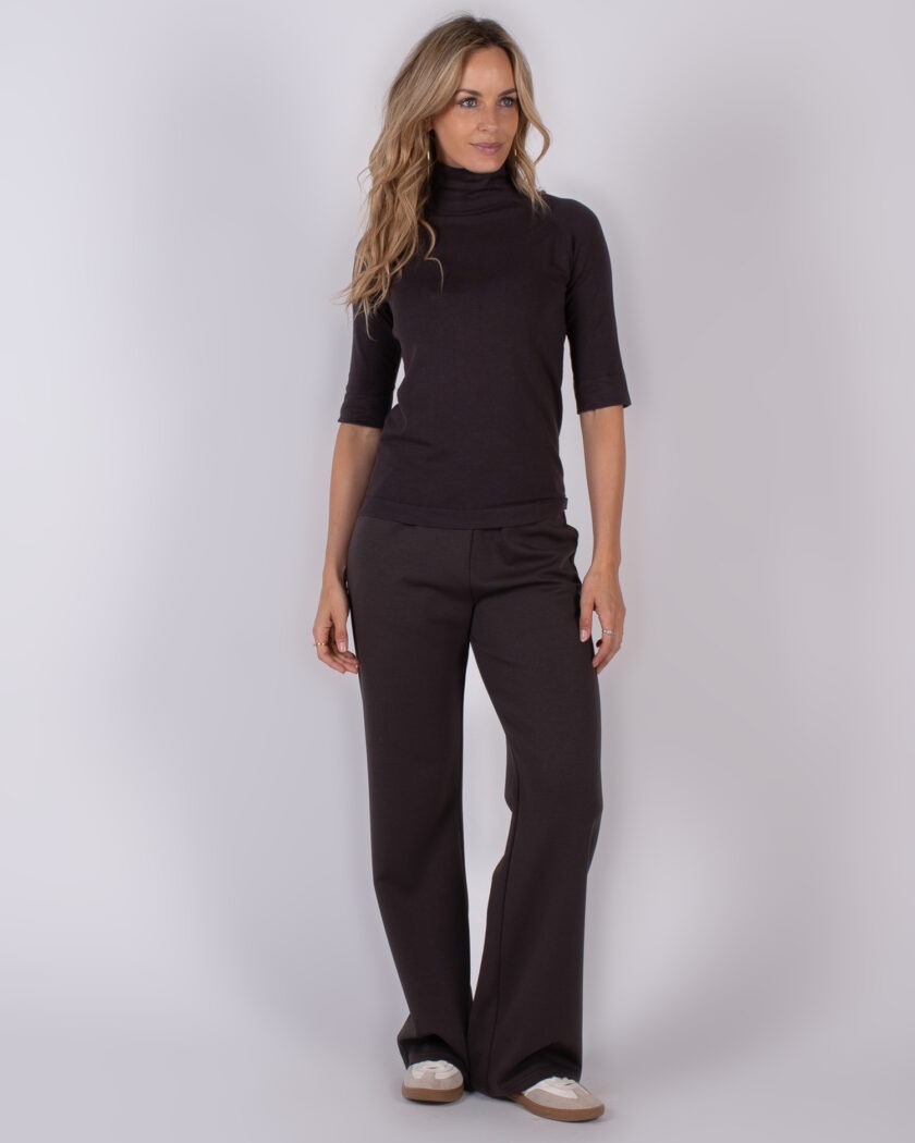 Vrouw draagt een donkerbruine coltrui met halve mouwen en bijpassende wijde broek uit de Studio AW25-26 collectie.