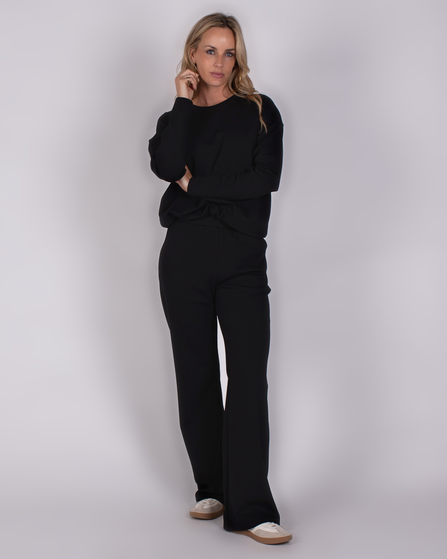 Vrouw draagt een zwarte Studio AW25-26 broek met bijpassende top en witte sneakers.