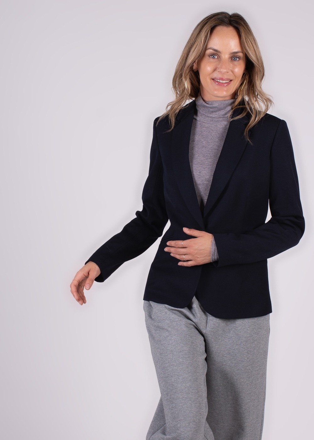 Een vrouw draagt een donkerblauwe Nikko blazer over een grijze coltrui, gecombineerd met een grijze broek, op een lichte achtergrond.