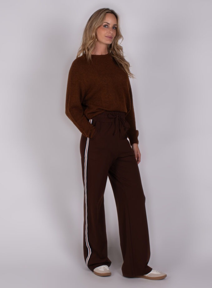 Vrouw draagt een bruine trui en wijde bruine broek met witte strepen in Studio_AW25-26-119.