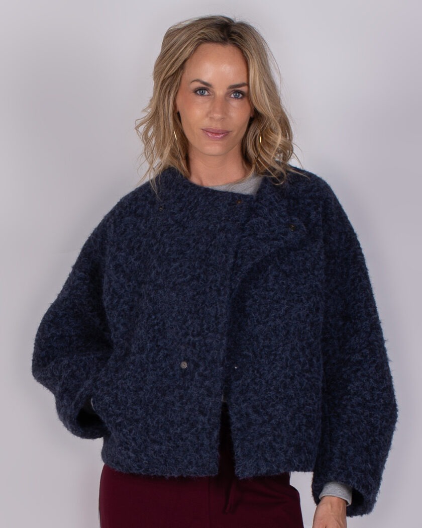 Vrouw poseert in een donkerblauwe, wollige jas uit de Studio AW25/26 collectie tegen een neutrale achtergrond.