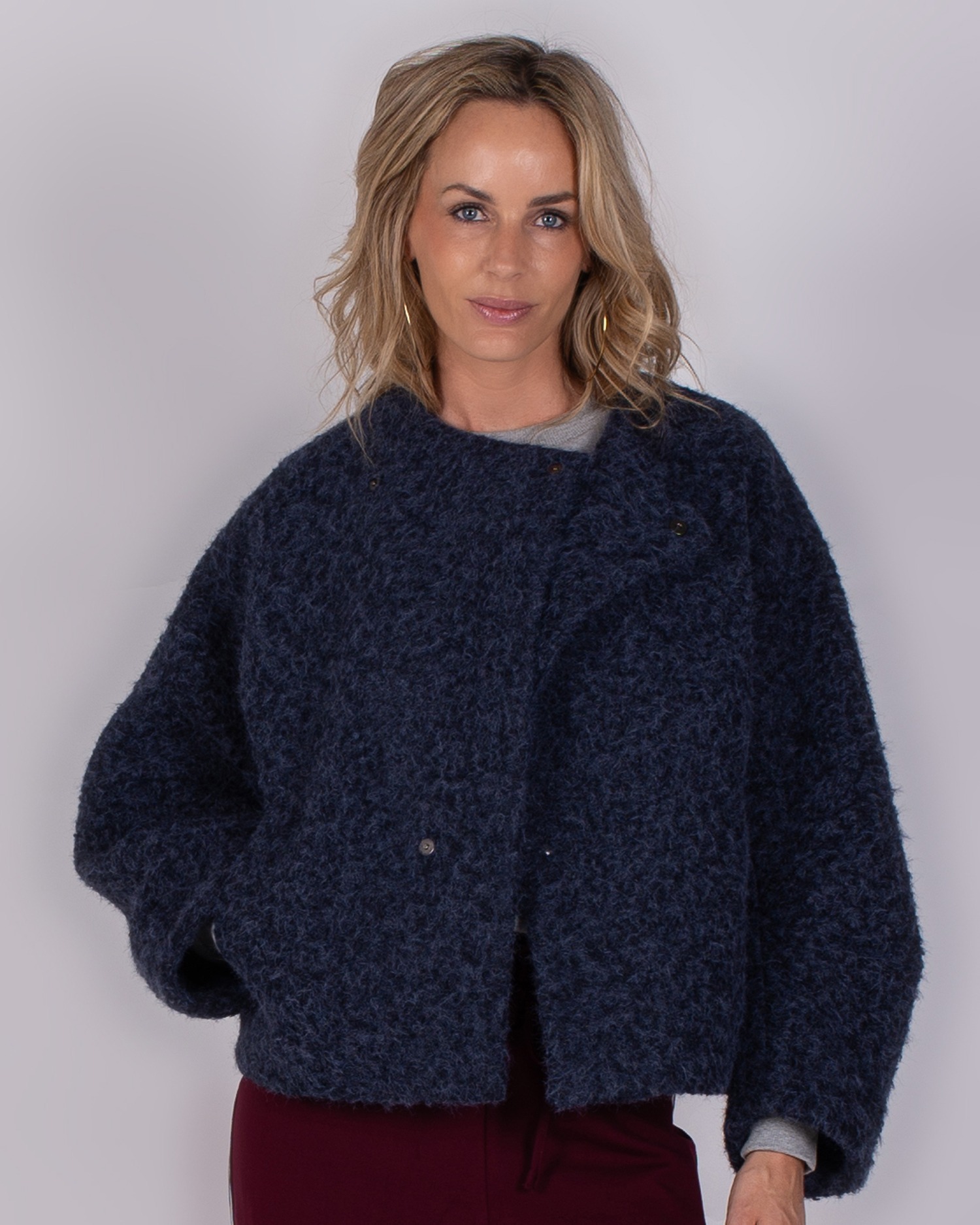 Vrouw poseert in een donkerblauwe, wollige jas uit de Studio AW25/26 collectie tegen een neutrale achtergrond.