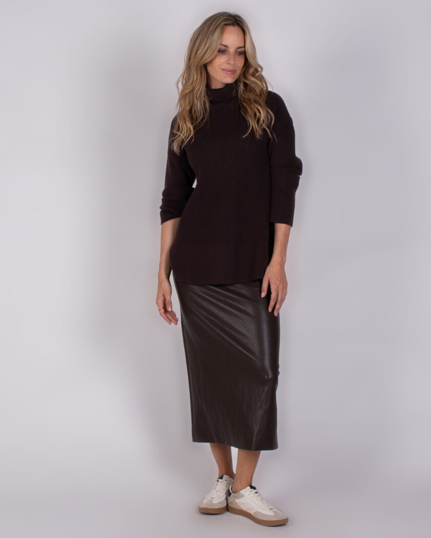 Vrouw draagt een donkerbruine coltrui met een donkerbruine midi-leren rok en witte sneakers uit de Studio AW25-26 collectie.