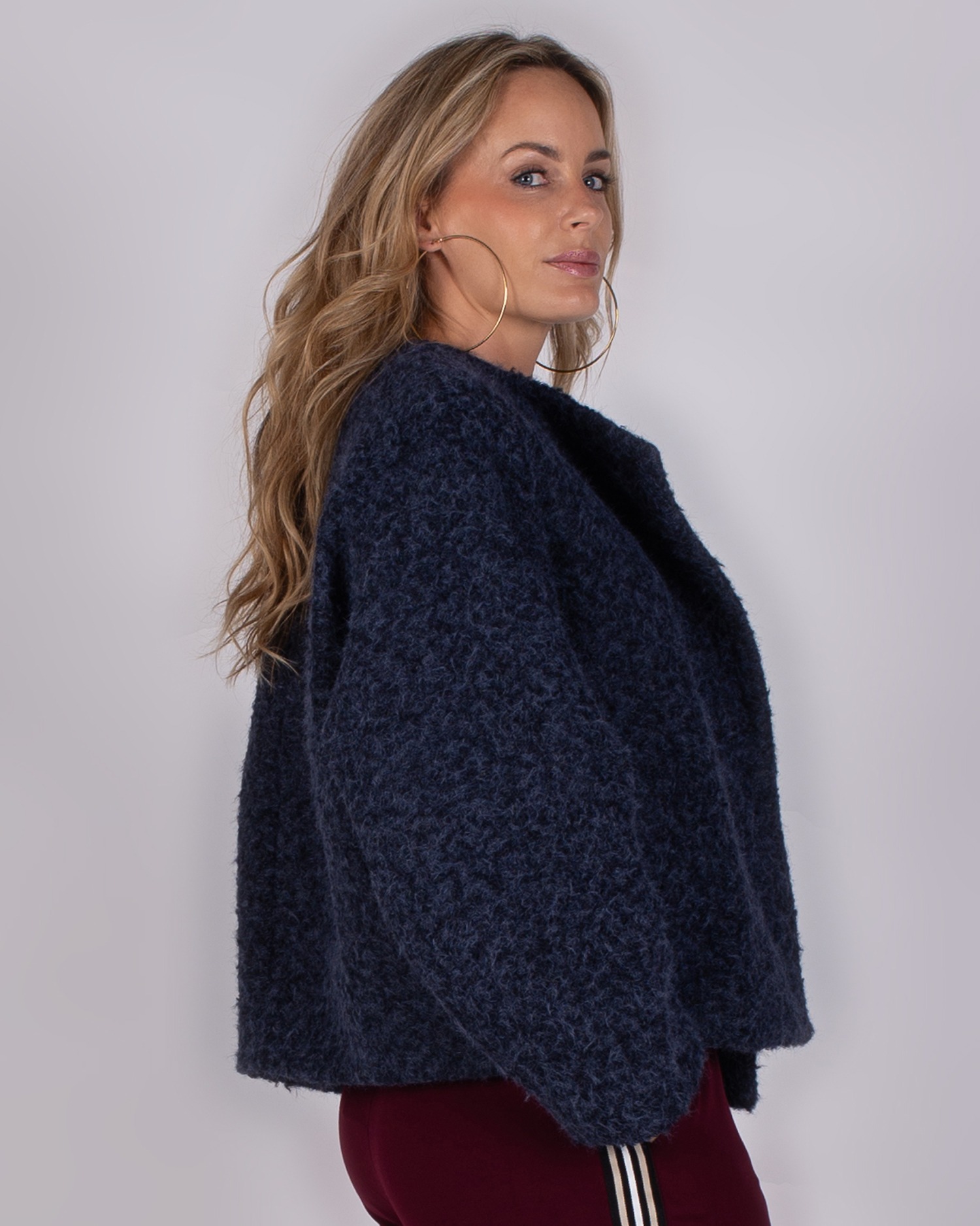 Studio_AW25-26-4 Vrouw in zijaanzicht draagt een donkerg blauwe, wollige jas uit de Studio AW25-26 collectie.