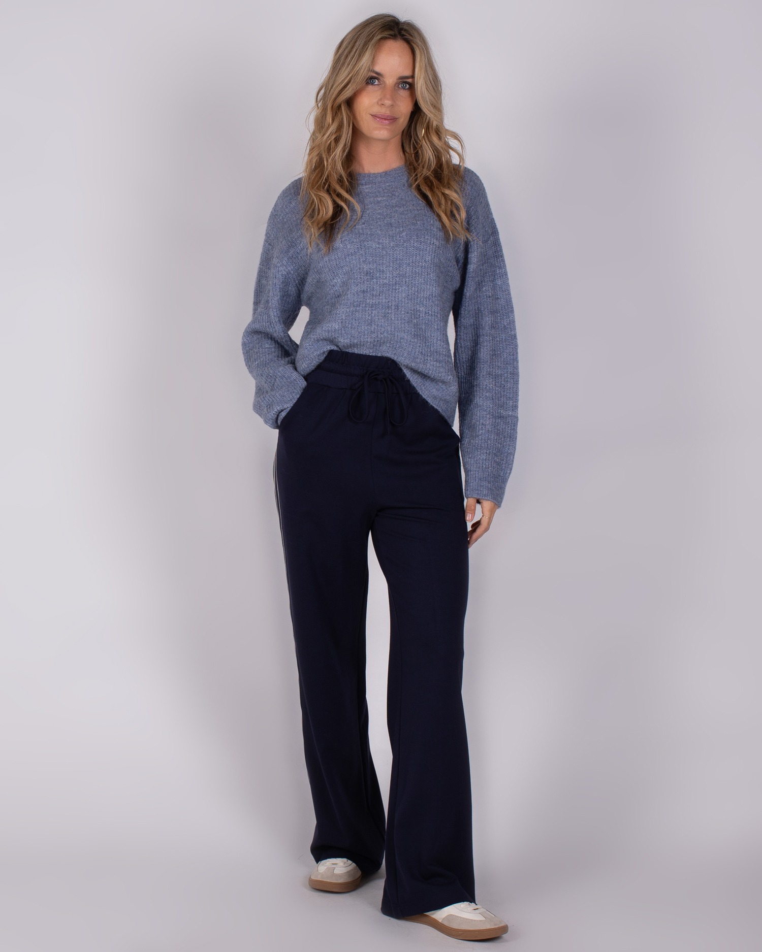 Vrouw draagt een blauwe trui en donkerblauwe wijde broek uit de Studio AW25-26 collectie.