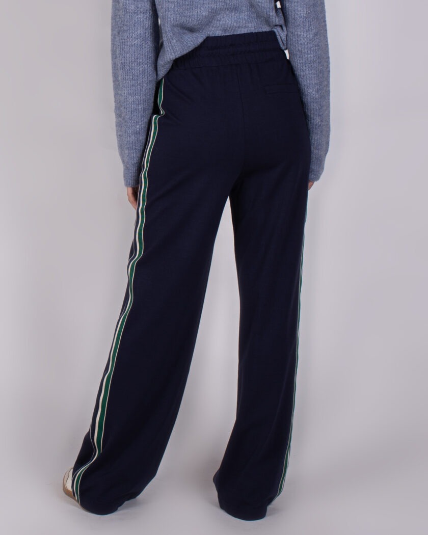 Achteraanzicht van een persoon in navy blauwe Studio AW25-26 broek met groene en witte zijstrepen.
