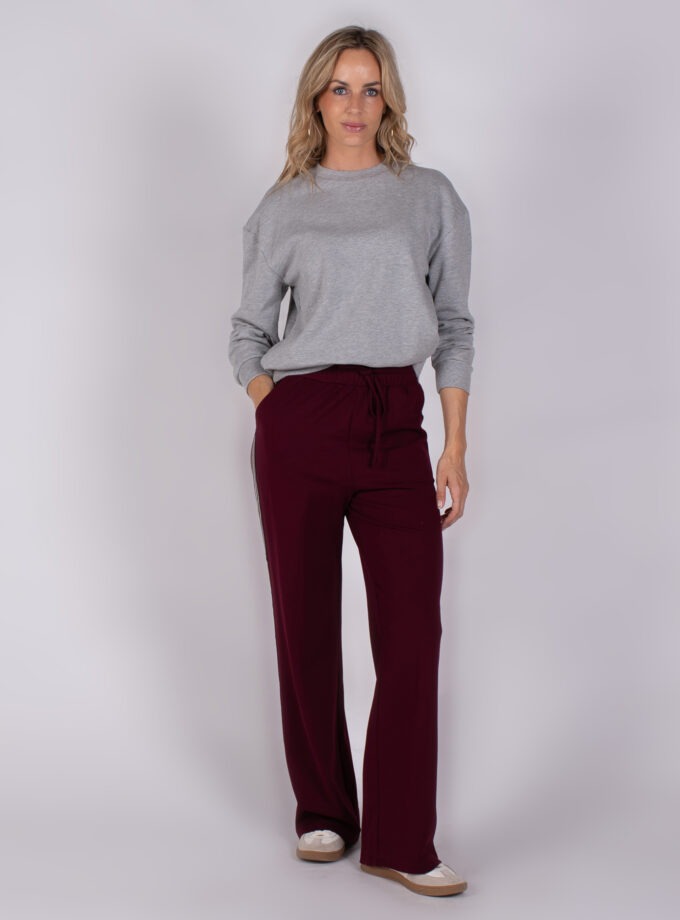 Vrouw in grijze trui en bordeauxrode wijde broek uit Studio AW25-26-6 collectie.