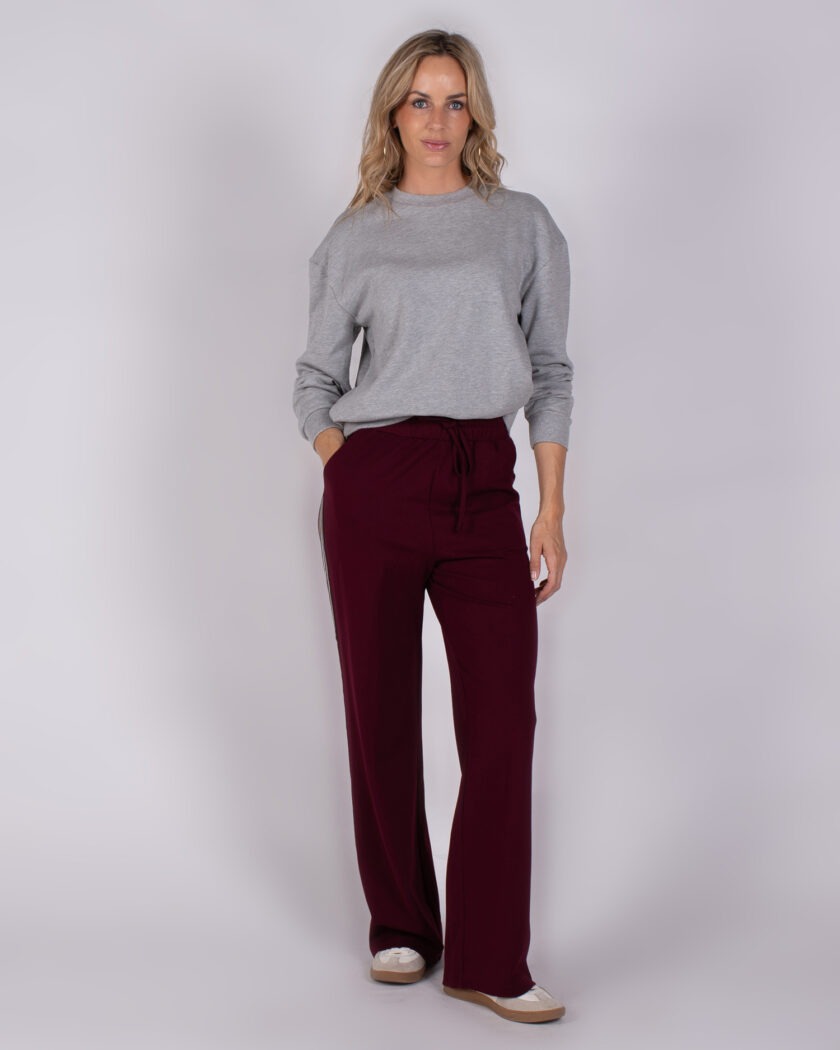 Vrouw in grijze trui en bordeauxrode wijde broek uit Studio AW25-26-6 collectie.
