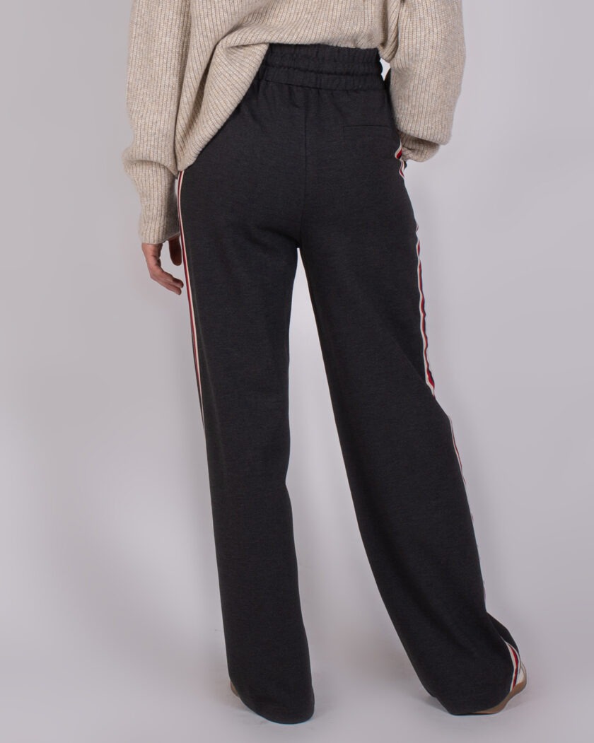 Achteraanzicht van een persoon in een beige trui en donkergrijze broek met gestreepte zijstrepen uit de Studio AW25-26 collectie.