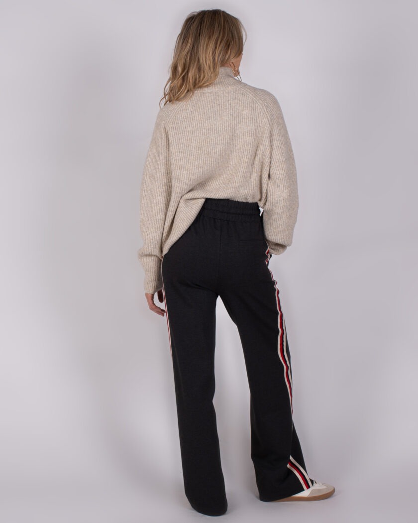 Vrouw gekleed in een beige coltrui en donkergrijze broek met sportieve strepen langs de zijkanten, gezien van achteren.