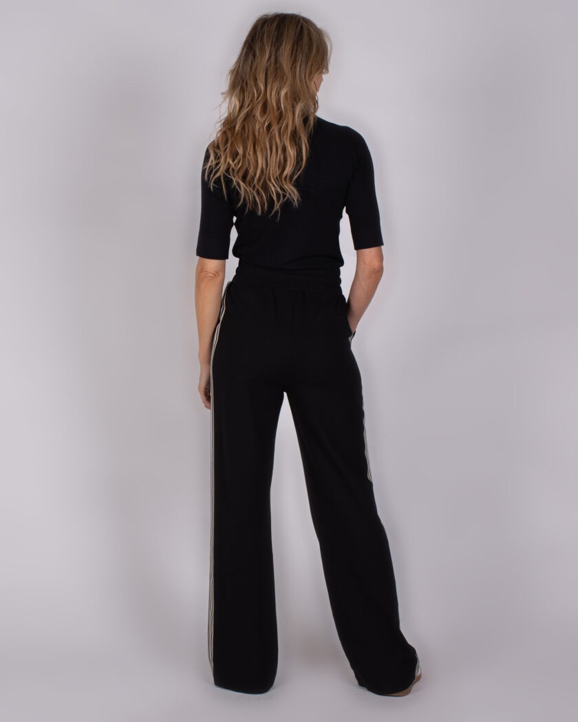Vrouw gekleed in een zwarte Studio AW25-26-73 outfit met wijde broek en halve mouwen, gezien van achteren.