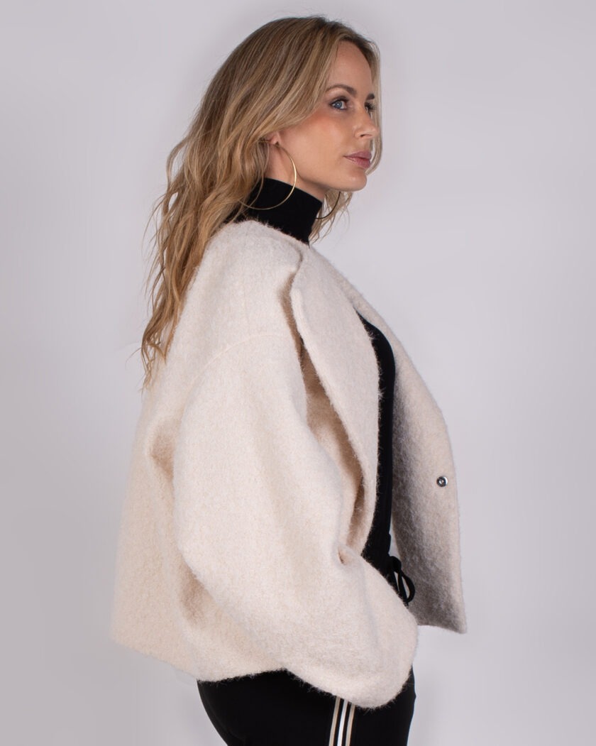 Vrouw met lang blond haar draagt een oversized crèmekleurige jas uit de Studio AW25-26 collectie.