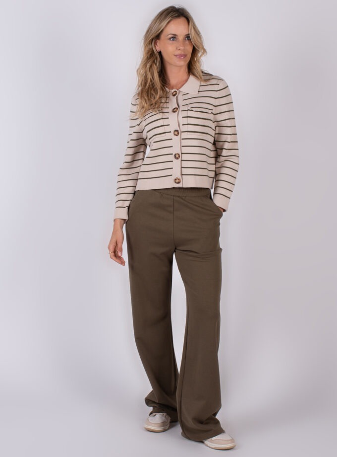 Vrouw draagt een beige gestreept vest met grote knopen en olijfgroene broek met wijde pijpen.