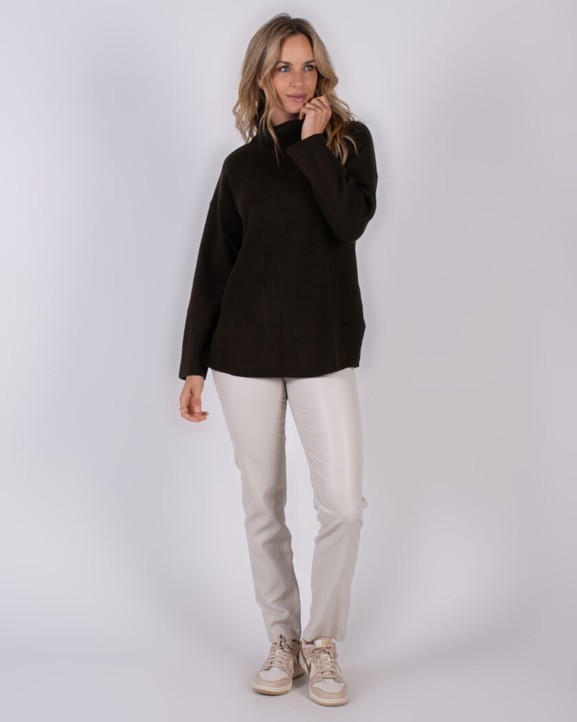 Vrouw draagt een donkerbruine trui en lichtgrijze broek uit de Studio AW25-26 collectie.