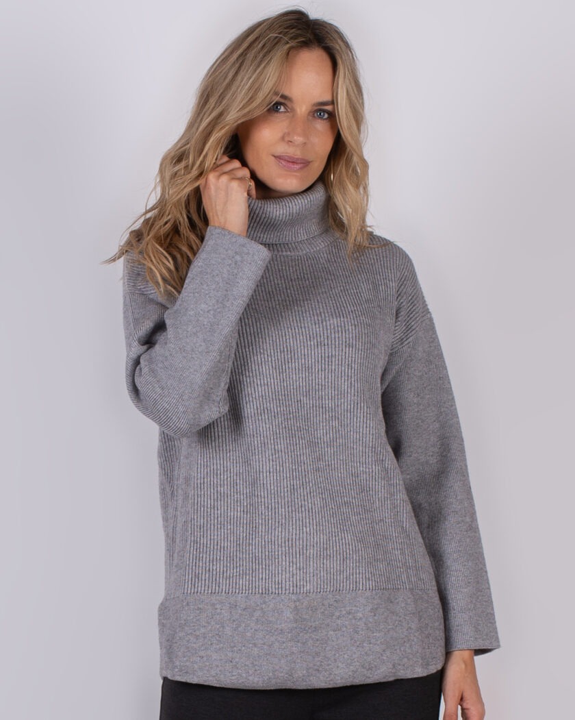 Vrouw draagt een grijze, geribde coltrui uit de Studio AW25-26 collectie.