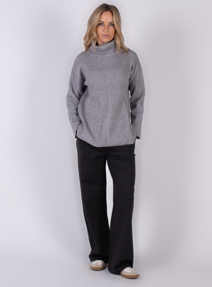 Vrouw in een grijze coltrui en donkere broek uit de Studio AW25-26 collectie.