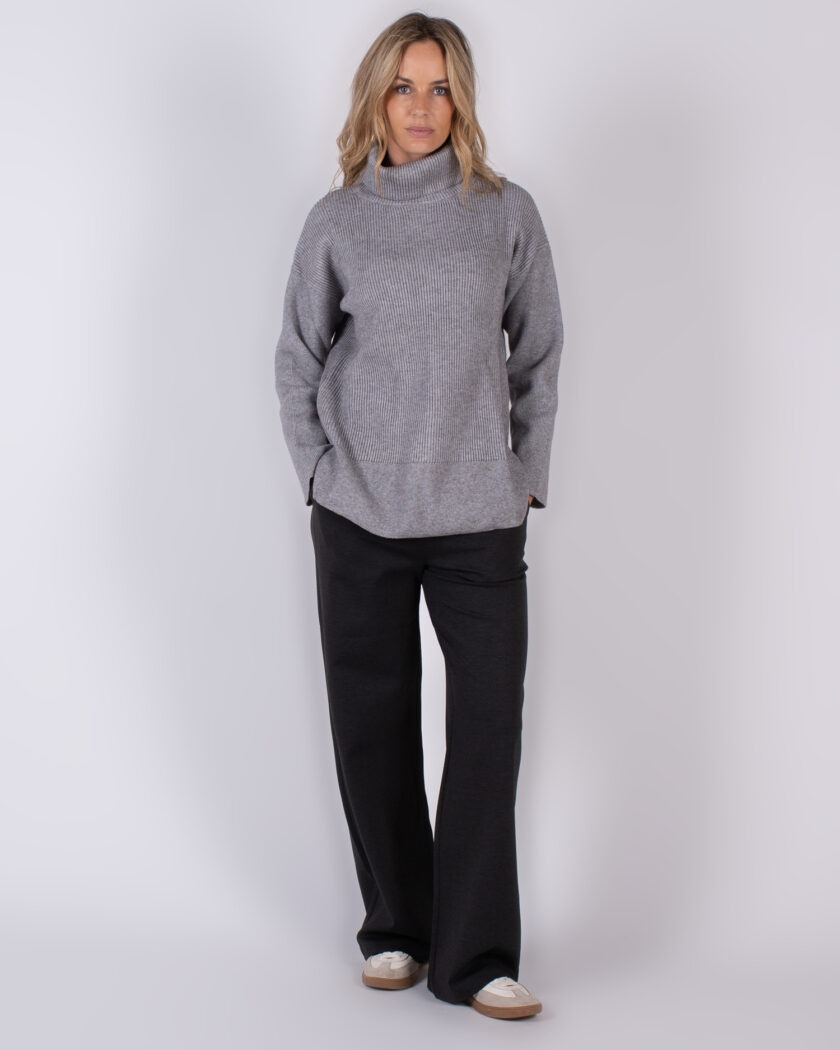 Vrouw in een grijze coltrui en donkere broek uit de Studio AW25-26 collectie.