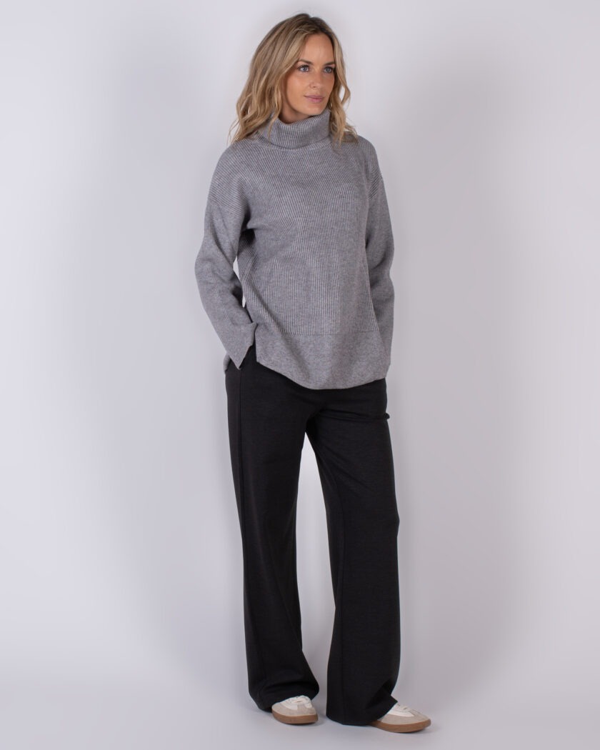 Vrouw draagt een grijze coltrui en zwarte wijde broek uit de Studio AW25-26 collectie.