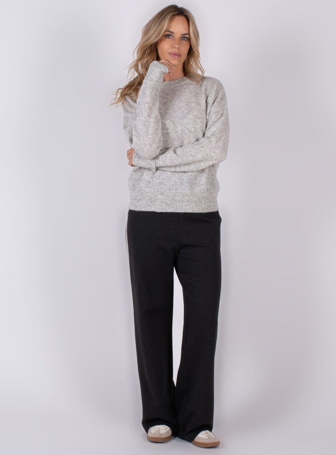Vrouw in comfortabele winteroutfit met een grijze trui en donkere wijde broek uit Studio AW25-26 collectie.