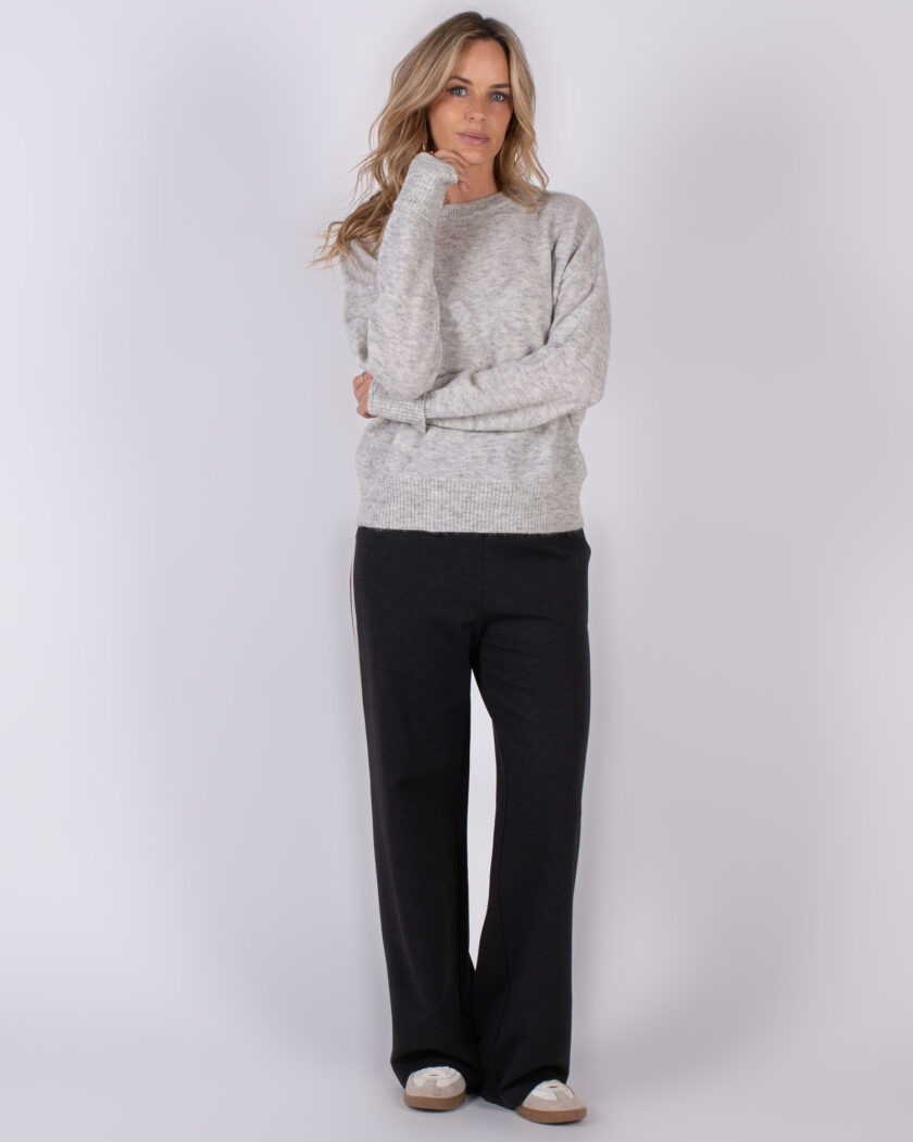 Vrouw in comfortabele winteroutfit met een grijze trui en donkere wijde broek uit Studio AW25-26 collectie.