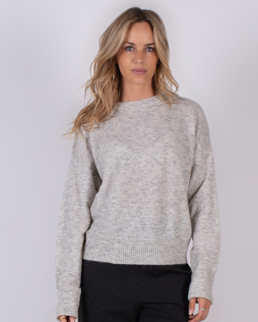Vrouw draagt een lichtgrijze, gemêleerde trui met ronde hals uit de Studio AW25-26 collectie.