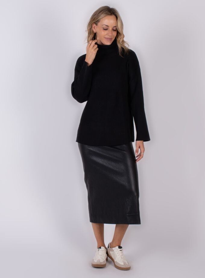Vrouw draagt een zwarte coltrui en een zwarte midi-rok van leerlook uit de Studio AW25-26 collectie.